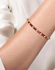 Red bracelet with gold accents on a person's wrist against a white background