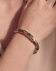 Close-up of a hand wearing a gold bracelet on a neutral background