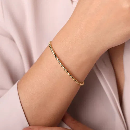 Gold bracelet on a person's wrist with a light pink background