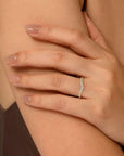 Hand wearing a gold and diamond curved ring on a neutral background