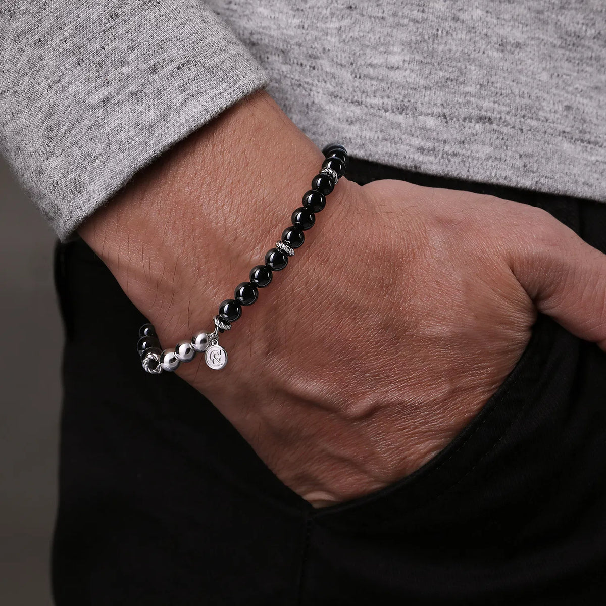 Person wearing a black beaded bracelet on a neutral background