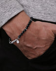 Person wearing a black beaded bracelet on a neutral background