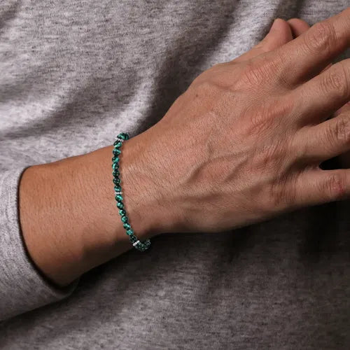 Hand wearing a green 4mm beaded bracelet on a gray background