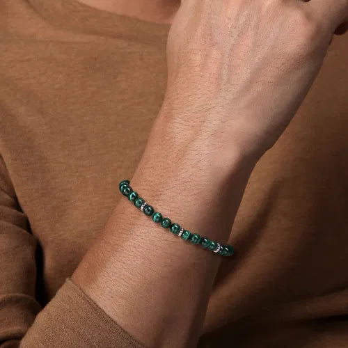 Close-up of a wrist wearing a green 6mm beaded bracelet against a brown background