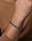 Close-up of a wrist wearing a green 6mm beaded bracelet against a brown background