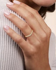 hand wearing curved yellow gold and diamond band on neutral background