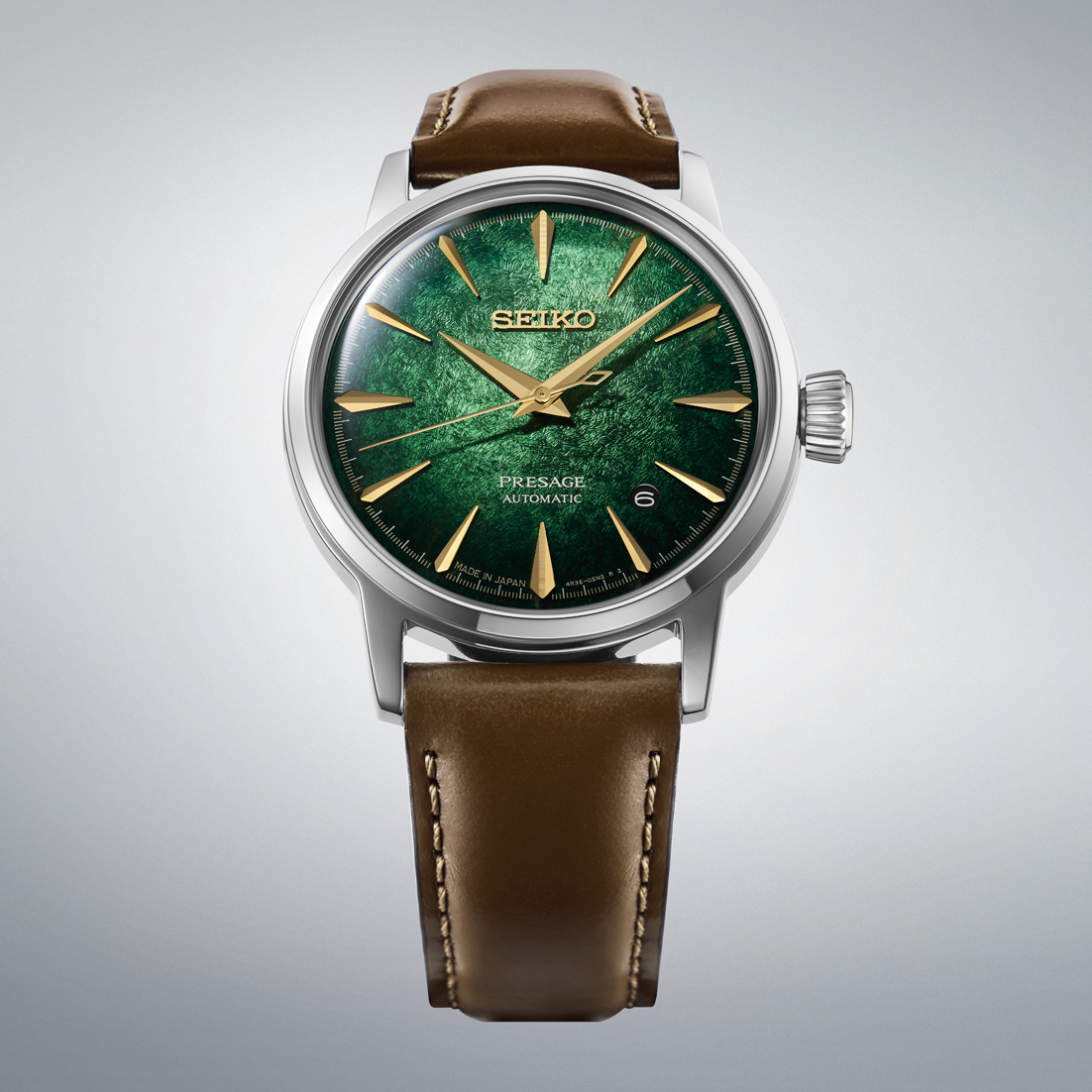 Seiko watch with green face and brown leather strap on gray background