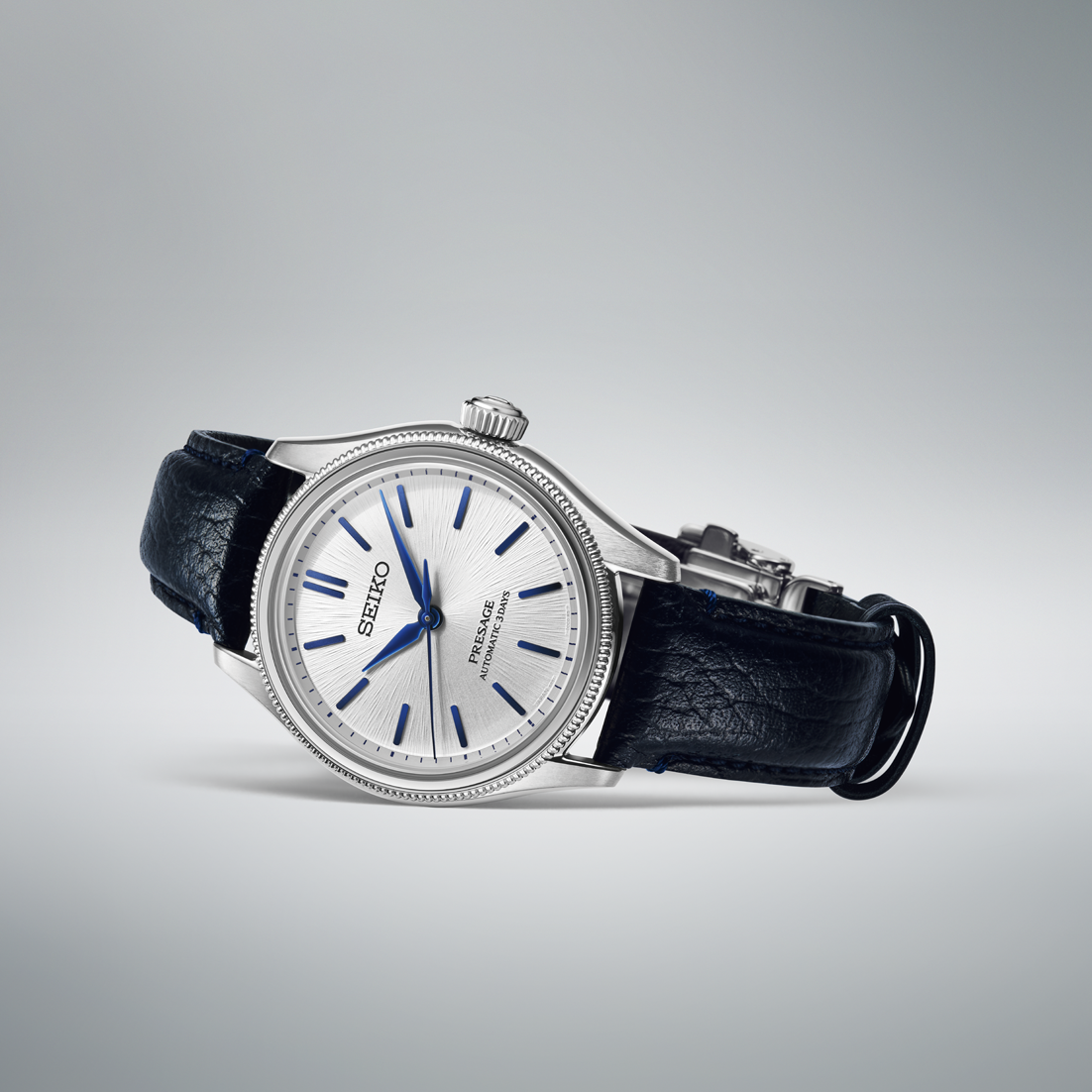 Seiko watch with black leather strap laying on its side on a gray background
