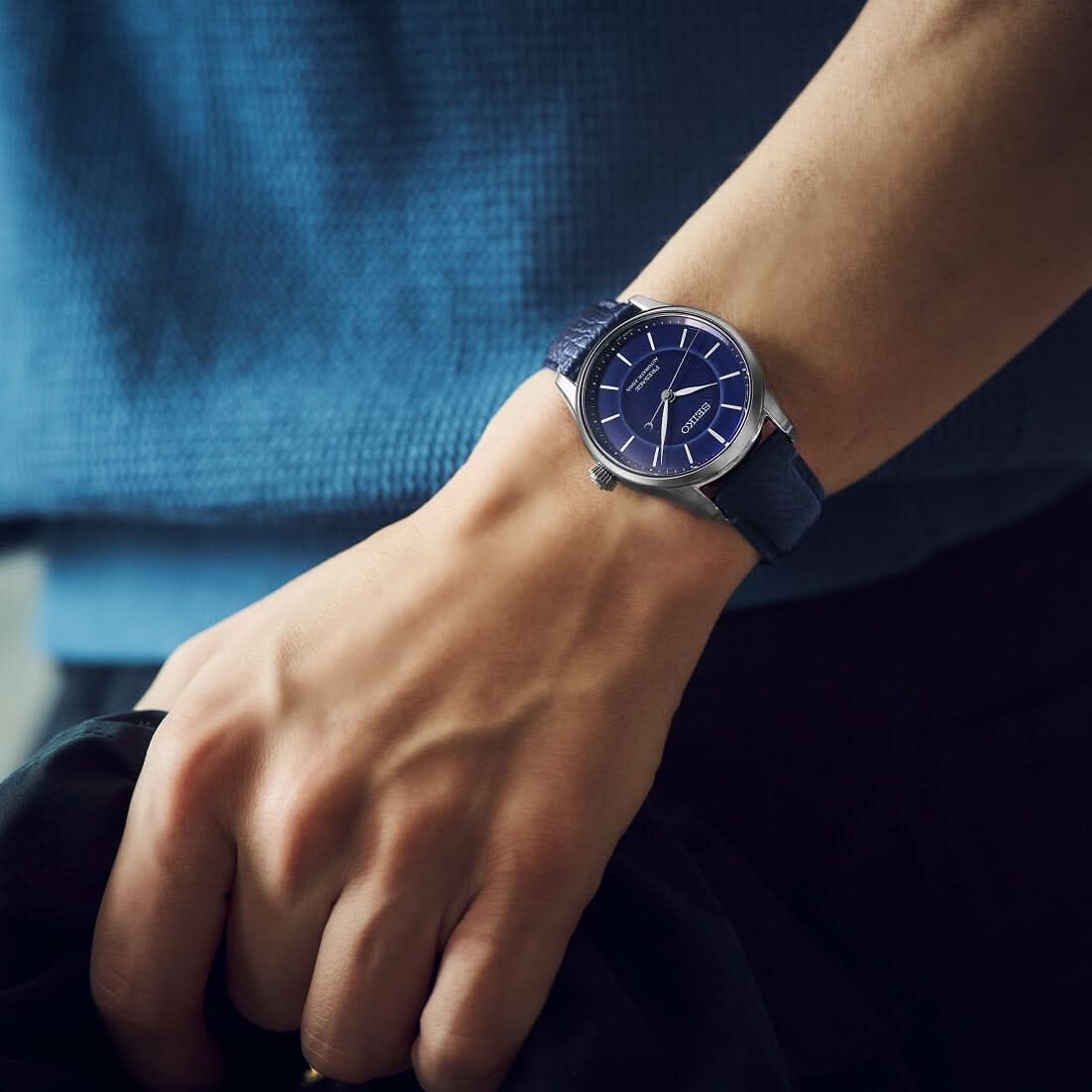 Person wearing a blue wristwatch with a blurred background