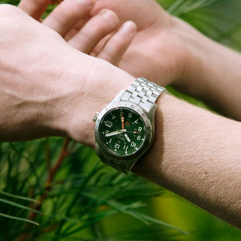 Close-up of a wrist wearing a green watch with a blurred natural background