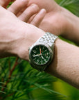 Close-up of a wrist wearing a green watch with a blurred natural background