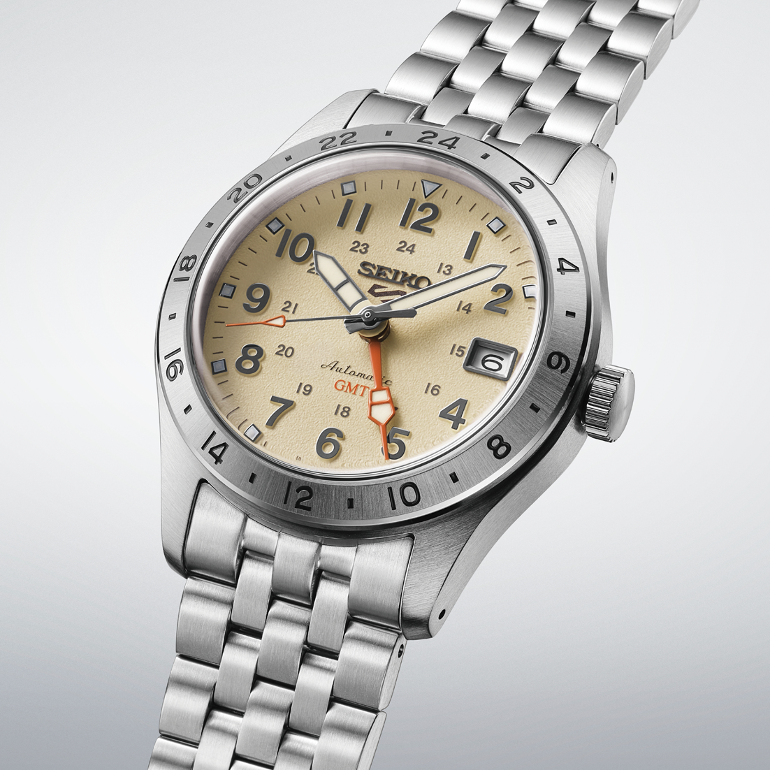 A Seiko wristwatch with a stainless steel link bracelet, featuring a beige dial with black Arabic numerals, a silver bezel, and a date window.- angled