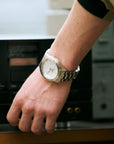 Hand wearing a gold watch with a blurred background