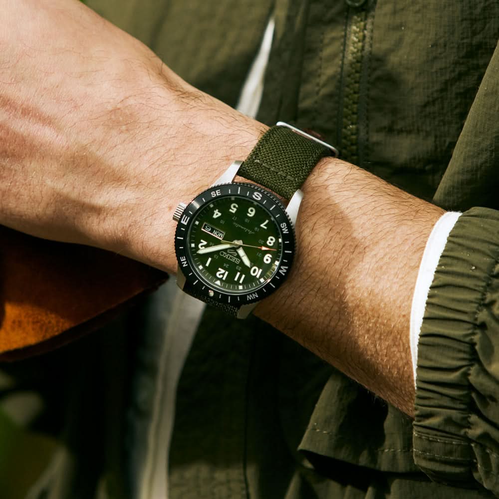 Person wearing a green watch with a matching watch and jacket outdoors
