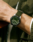 Person wearing a green watch with a matching watch and jacket outdoors