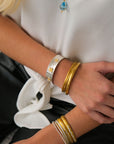 Close-up of a person's wrist wearing multiple gold bracelets with a white shirt in the background.