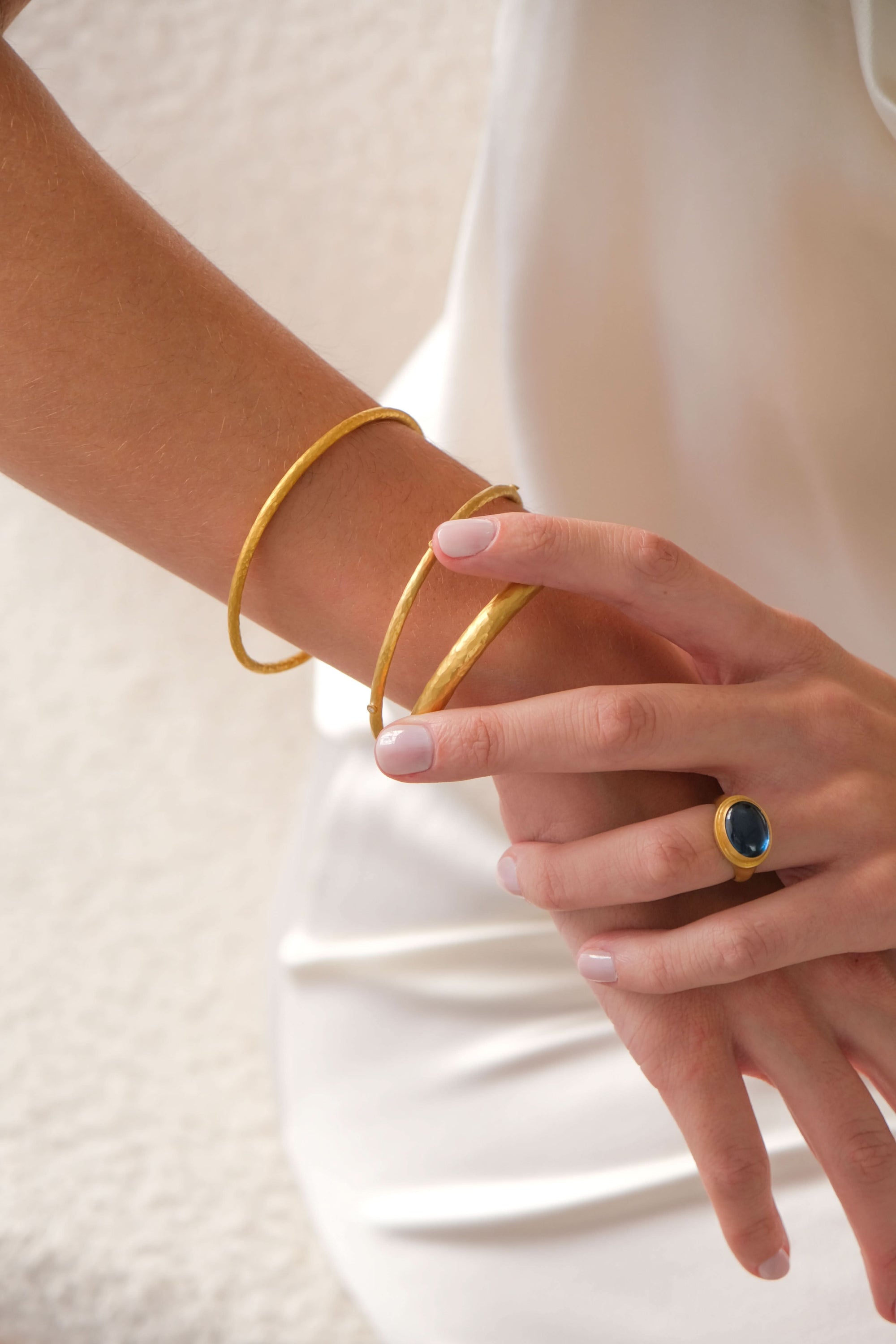 Gold bracelet and ring on a person's wrist and finger against a white background