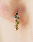 A close-up of a person's ear wearing a gold ear cuff with three small round gemstones in blue, green, and yellow tones.