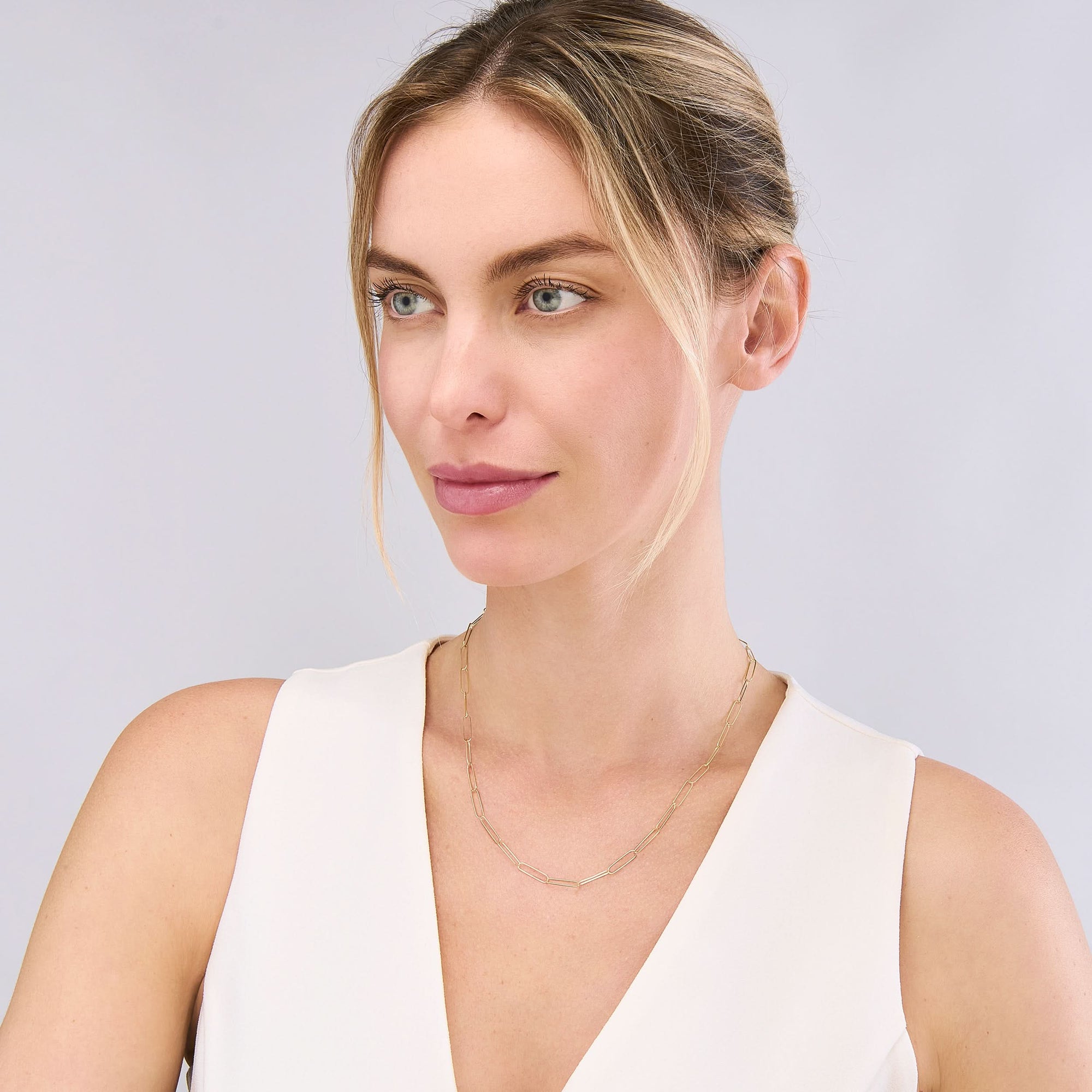 Woman wearing a white sleeveless top against a light gray background wearing a lightweight gold chain.