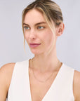 Woman wearing a white sleeveless top against a light gray background wearing a lightweight gold chain.