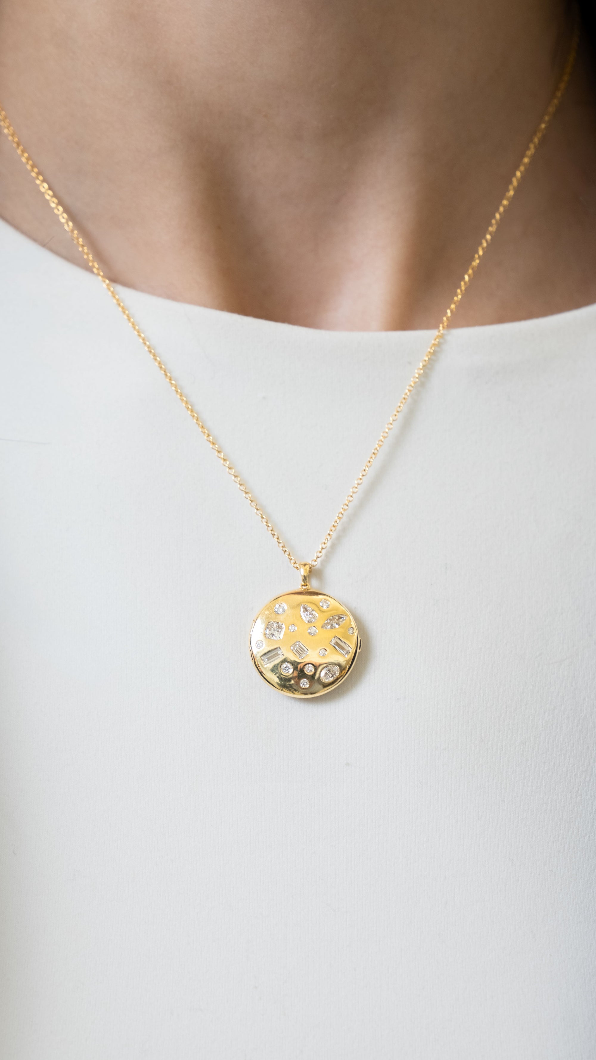 close up of a neck wearing a gold necklace with a round locket with multi shaped diamonds on a white background