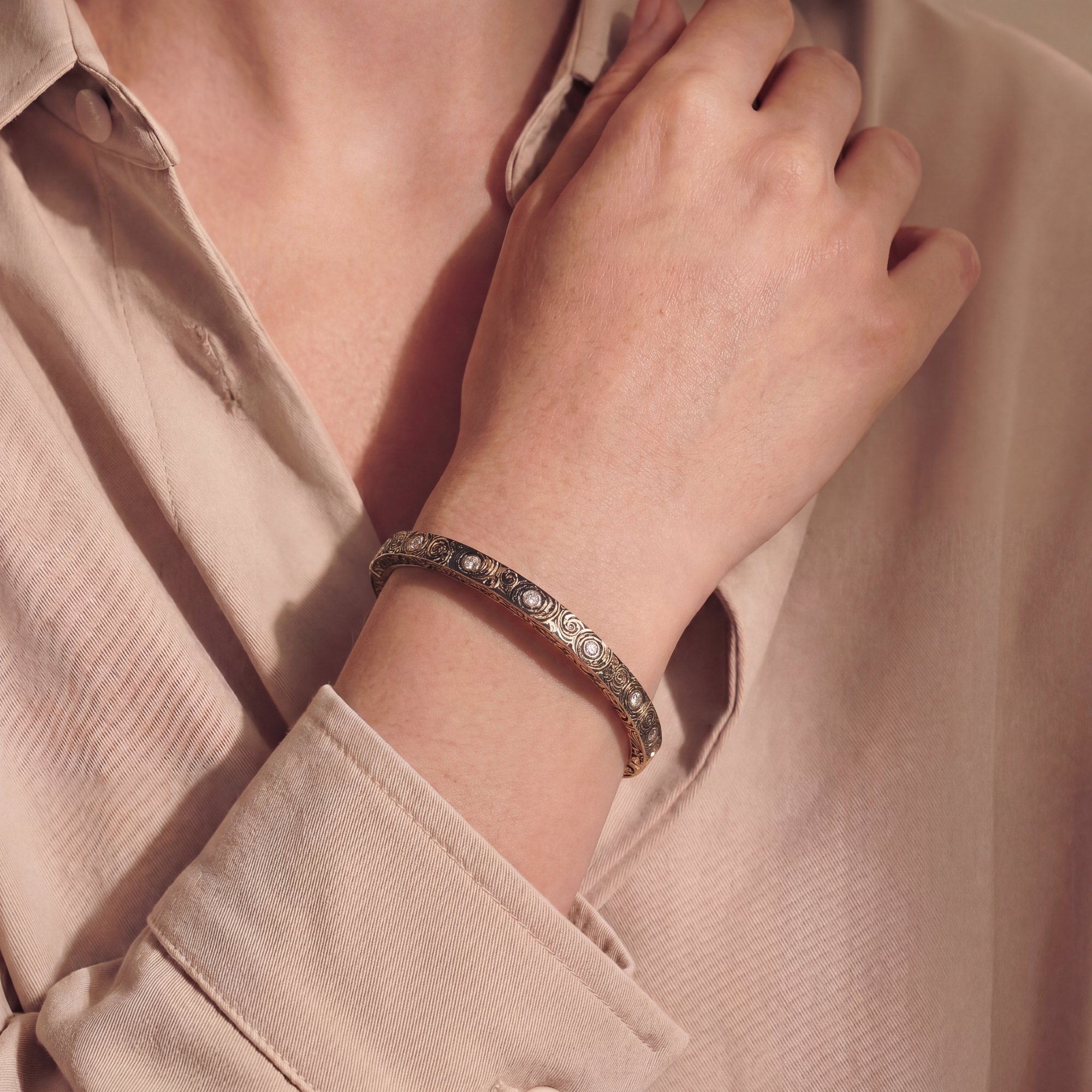 close up of an arm with a gold and black swirled bracelet with embedded diamonds on a beige background 