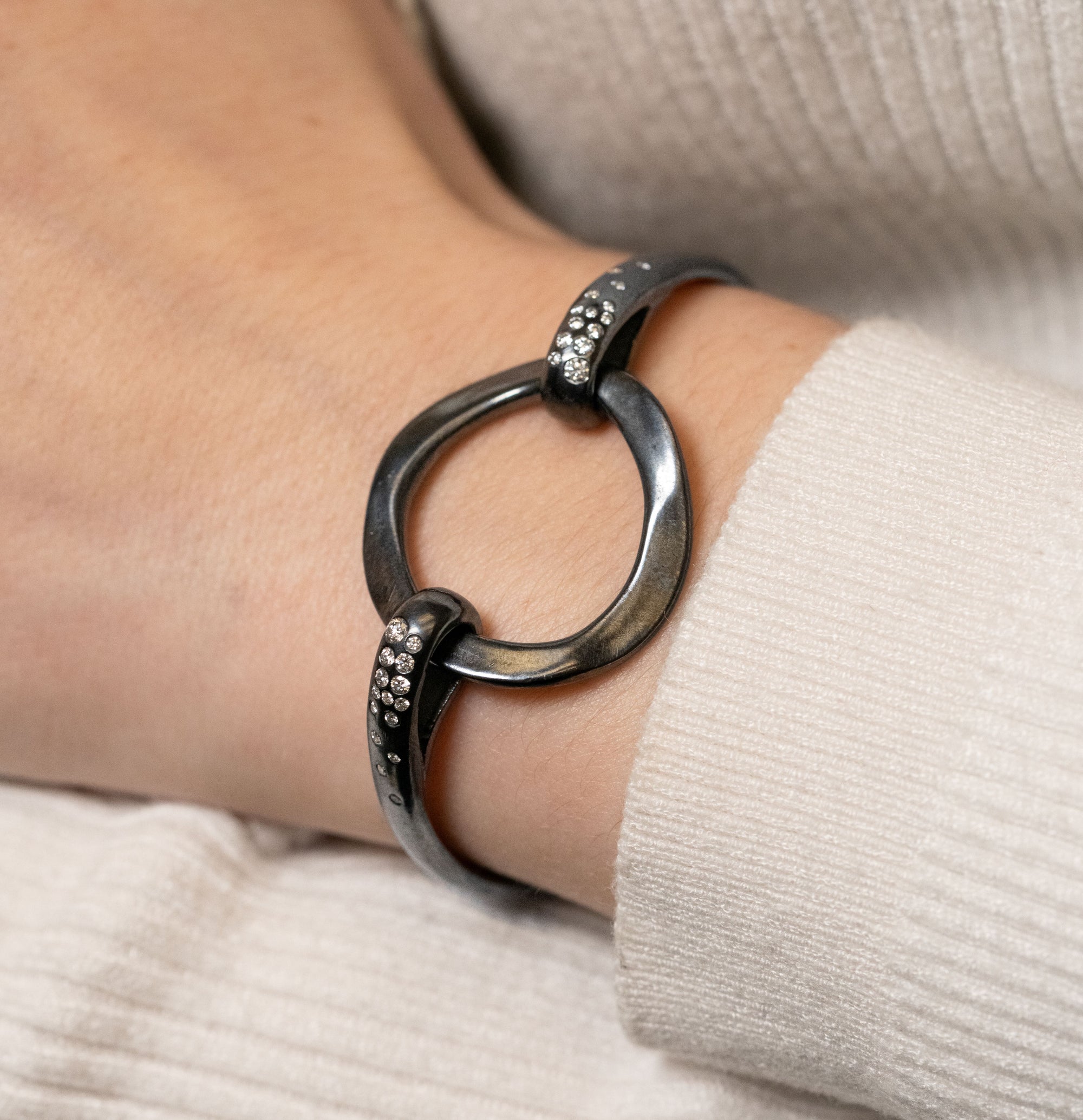 black bracelet with embedded diamonds and a large center circle on a wrist with a cream sweater background.