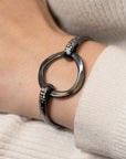 black bracelet with embedded diamonds and a large center circle on a wrist with a cream sweater background.