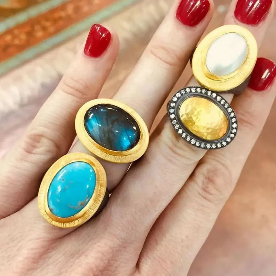 Four rings with different colored stones on a hand with red nail polish.