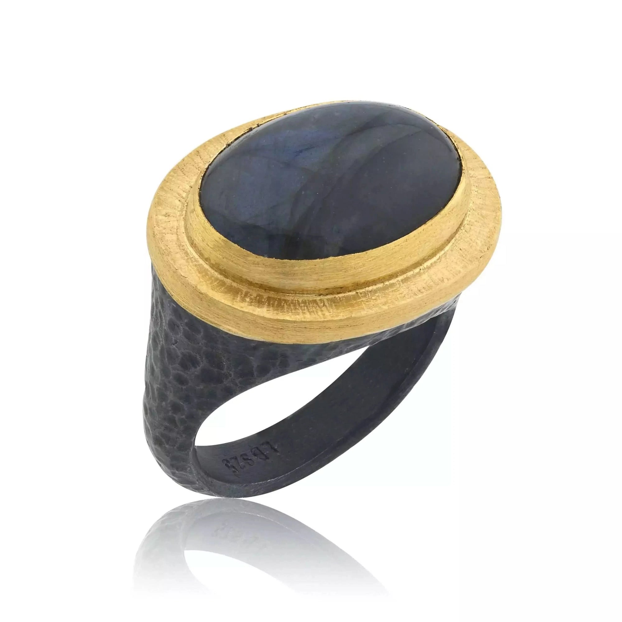 A hand-wrought Lika Behar Pompei statement ring, featuring an east-west oval cabochon labradorite displaying shifting blue and gray flashes, bezel-set in rich 24k yellow gold with a hammered oxidized sterling silver border.