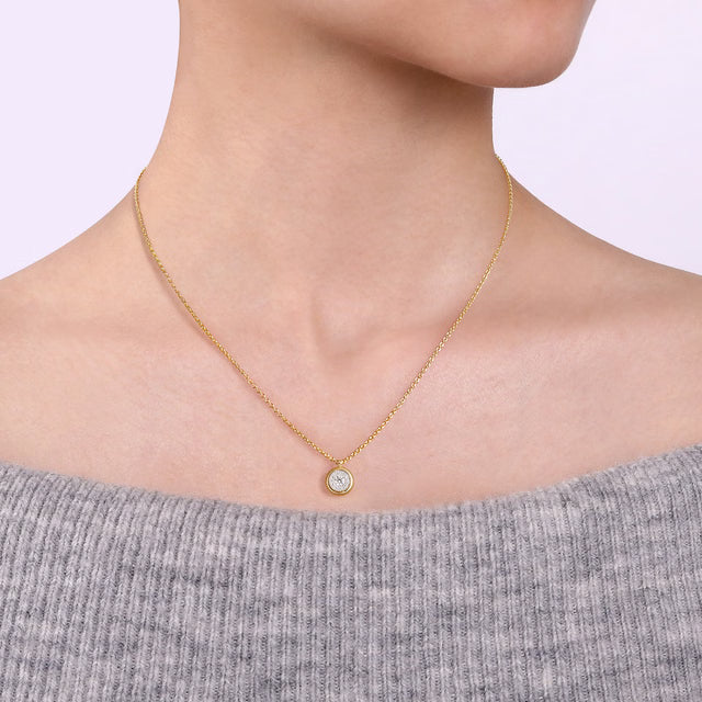 Gold necklace with a small round pendant worn by a person in a gray sweater.