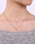 Gold necklace with a small round pendant worn by a person in a gray sweater.