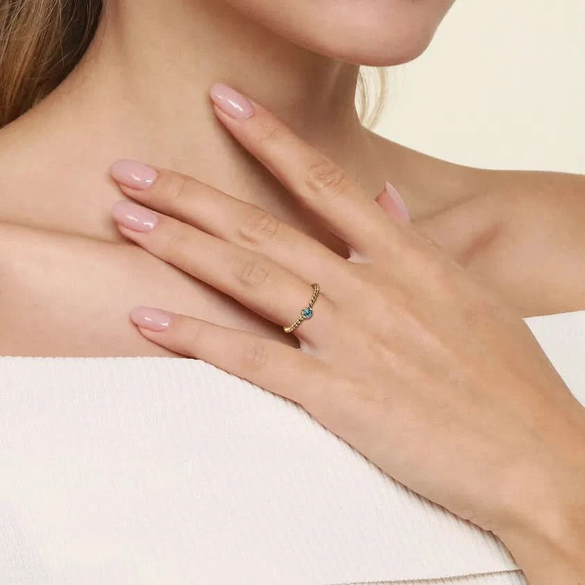 Close-up of a hand wearing a gold ring with blue gemstones, resting on a shoulder.