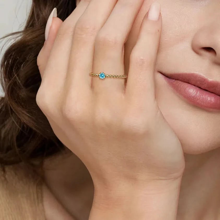 Close-up of a hand wearing a gold ring with a blue gemstone, touching the face.