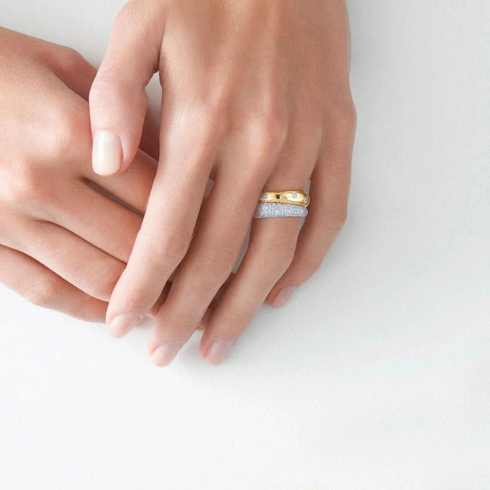 Close-up of a hand wearing a gold and silver ring on a light background