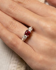 A close-up of a hand wearing a ring with a central square-cut red gemstone and clear side stones on a platinum band.