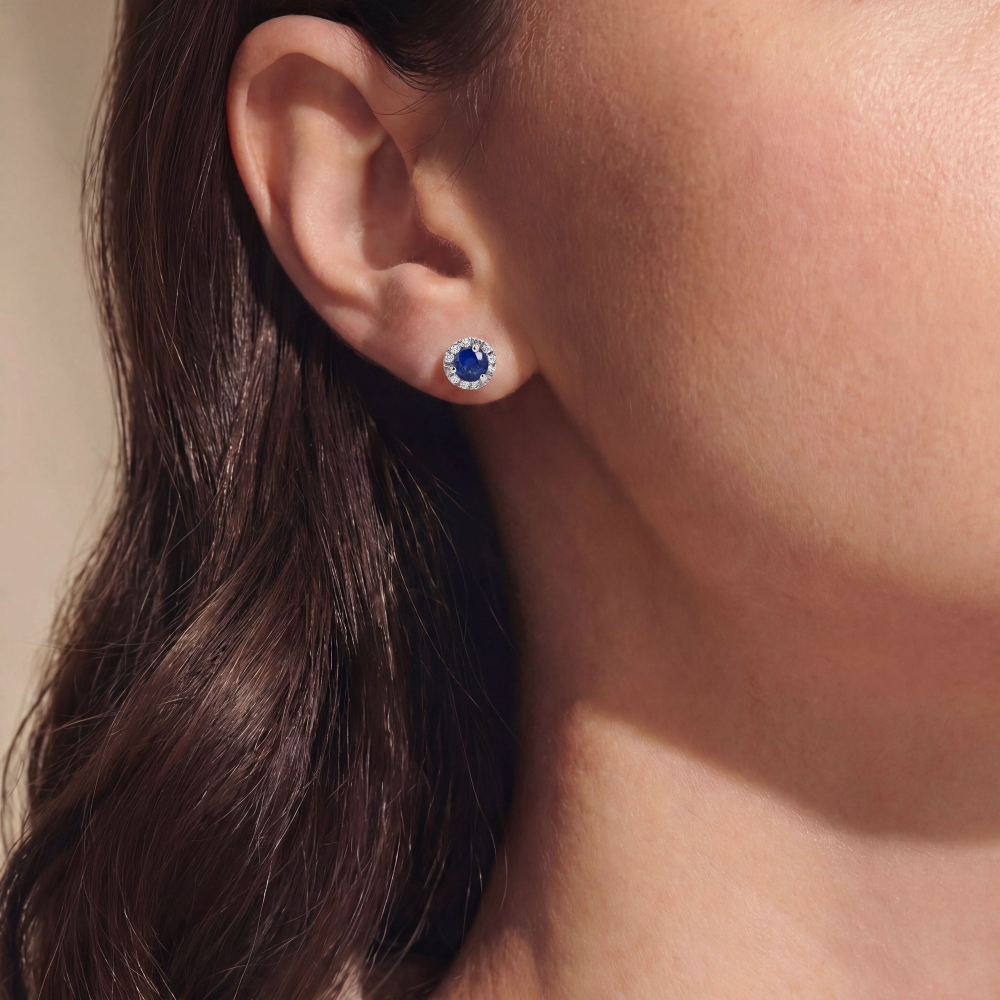 Close-up of an ear wearing a blue gemstone earring with diamonds with a blurred background