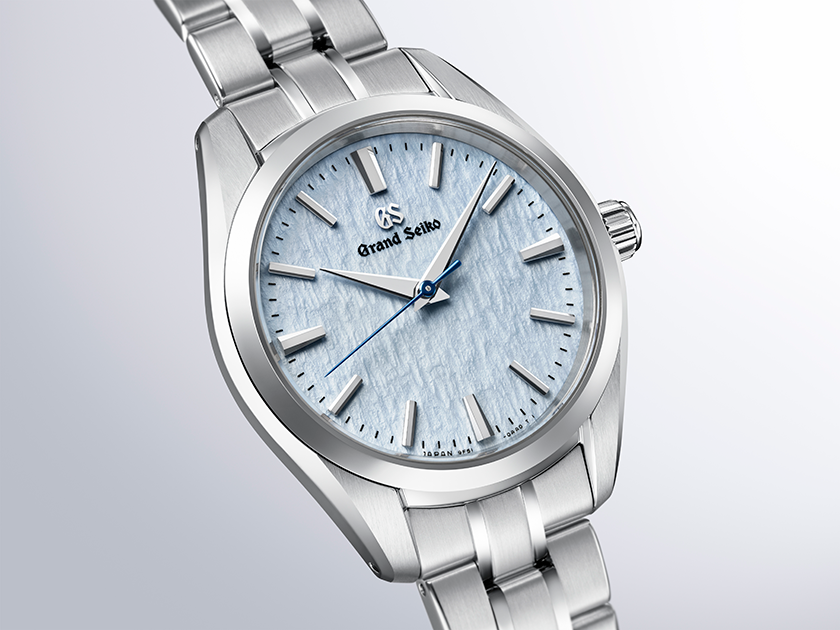 Silver watch with a light blue face on a light gray background angled 