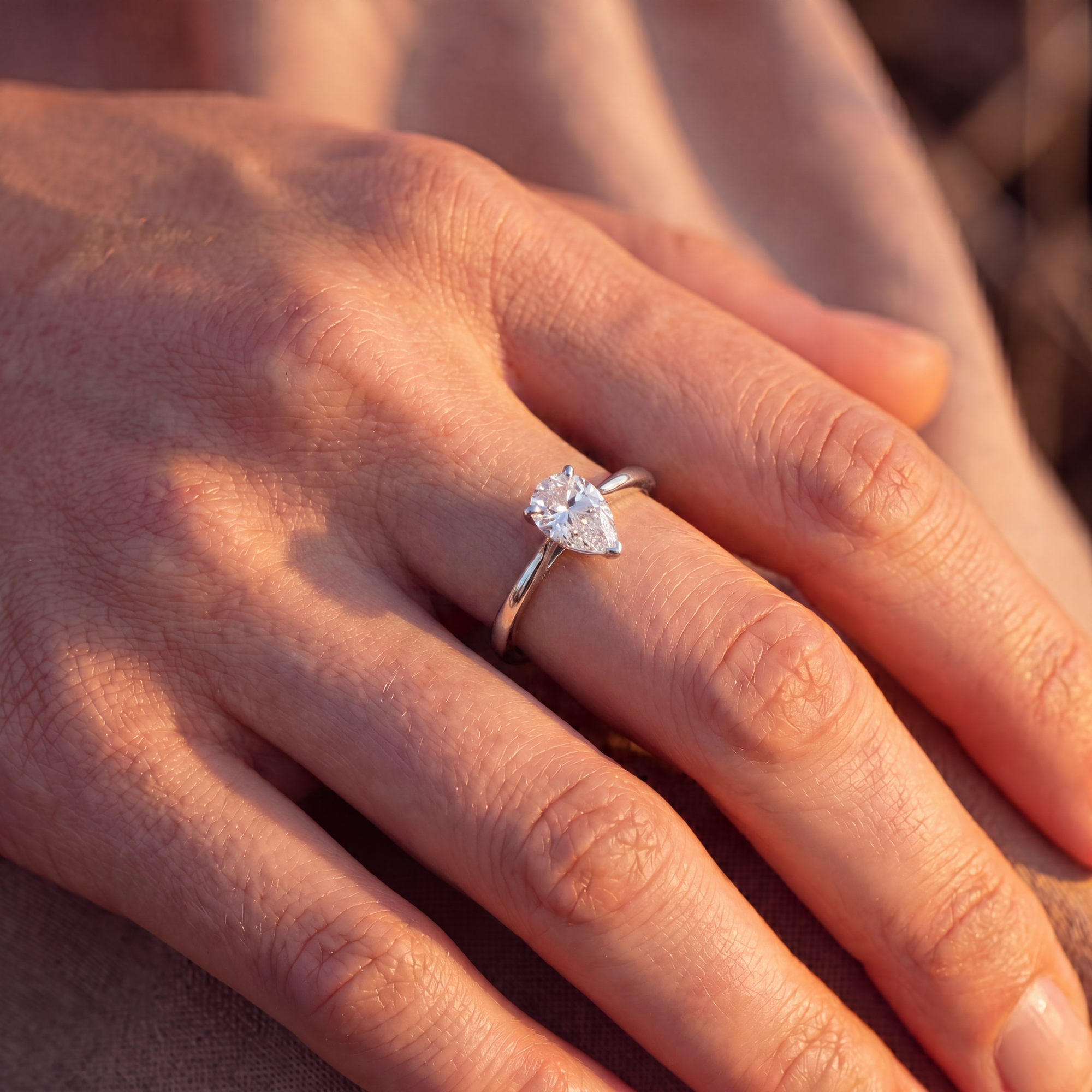 Close-up of a hand wearing a pear shaped lab diamond ring with a blurred background