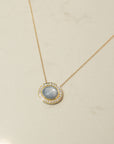 Gold necklace with an oval blue star sapphire  and diamond pendant on a beige background