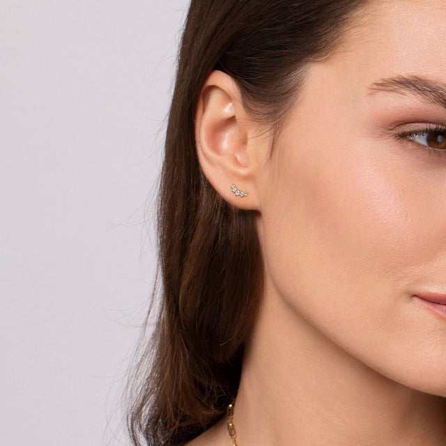 Close-up of a woman wearing diamond stud earrings with a plain background