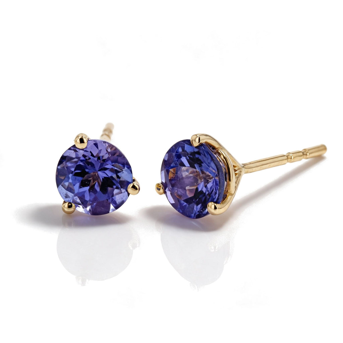 A pair of gold stud earrings with round-cut deep purplish blue tanzanite gemstones, shown on a clean white background with soft reflections.