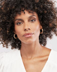 Woman with curly hair wearing gold hoop earrings against a white background