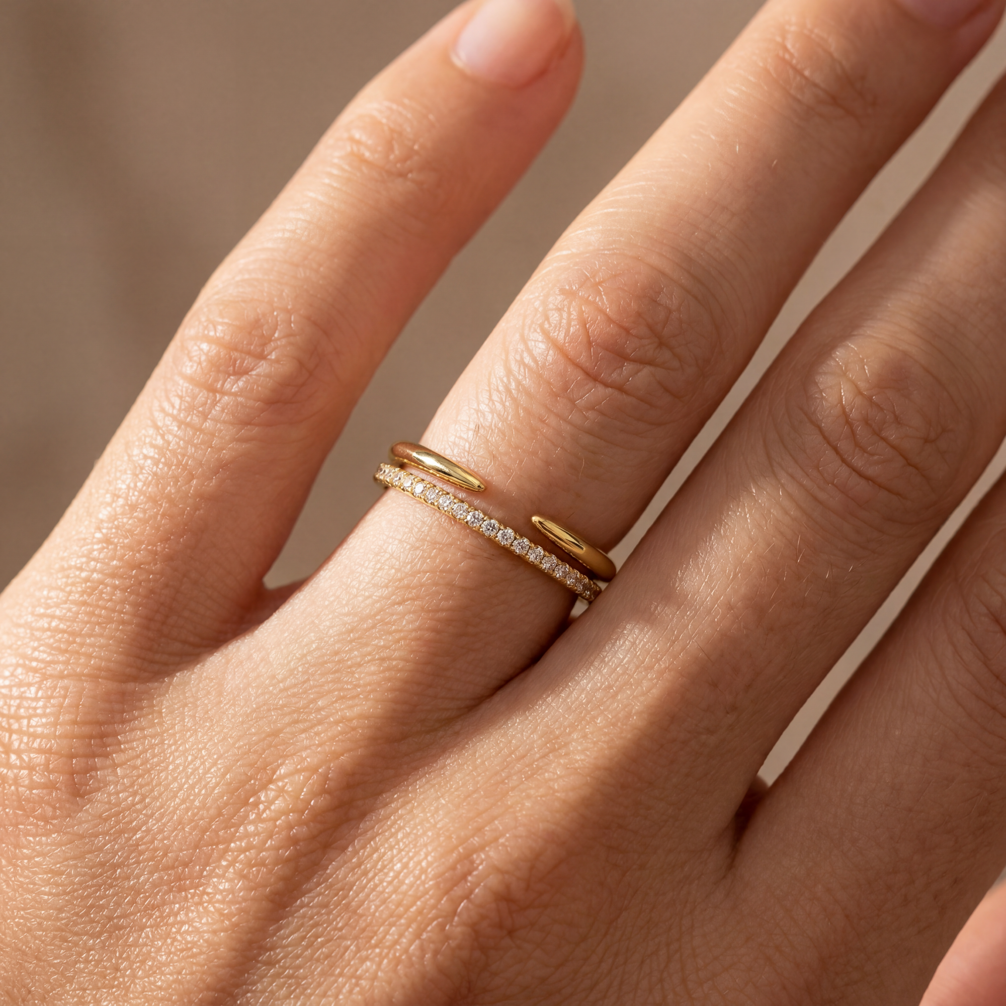 Close-up of a hand wearing a gold ring with diamond accents on a neutral background