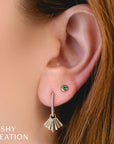 Close-up of an ear wearing a gold earring with a green gemstone, branded 'SHY CREATION'.
