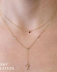 Gold necklace stack one with  red bezel and one with a cross pendant on a person's neck, branded 'SHY CREATION'.