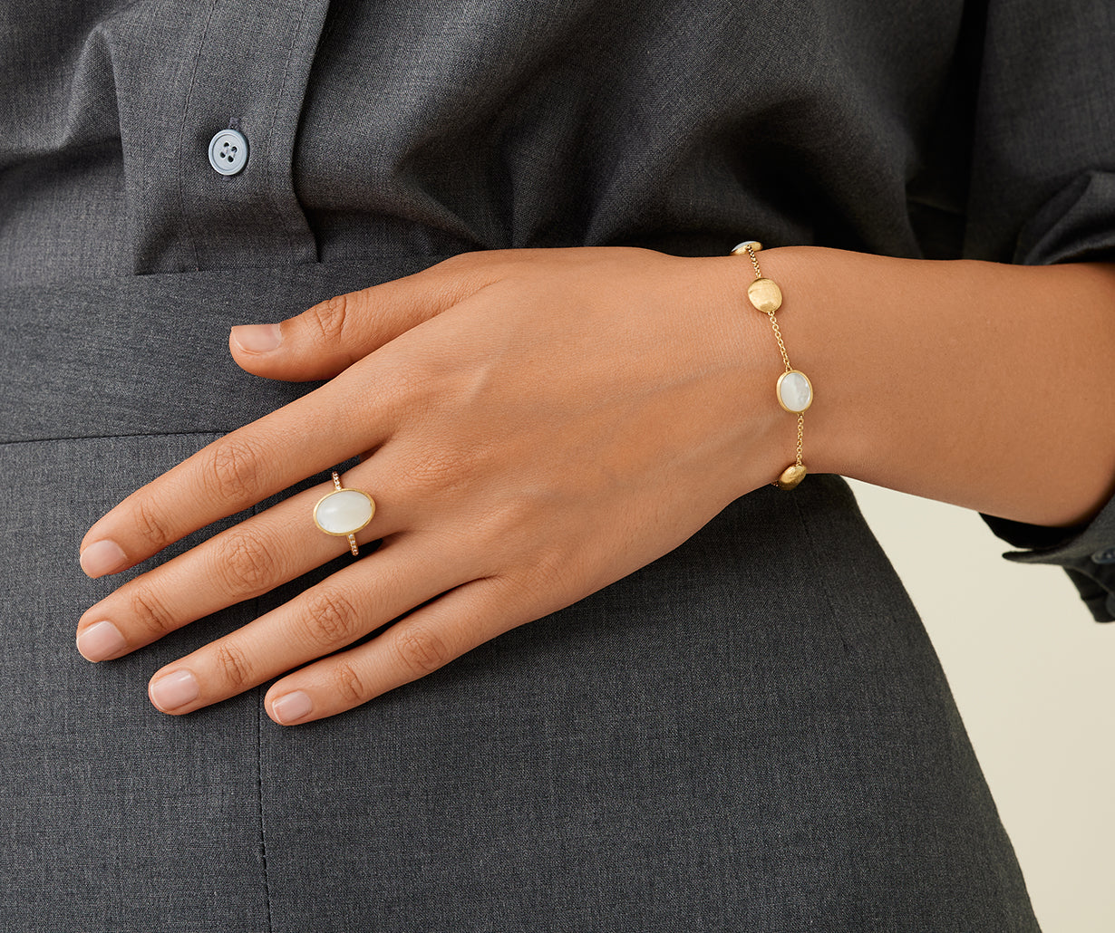 Hand wearing a gold bracelet and ring on a gray shirt background