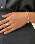 Hand wearing a gold bracelet and ring on a gray shirt background