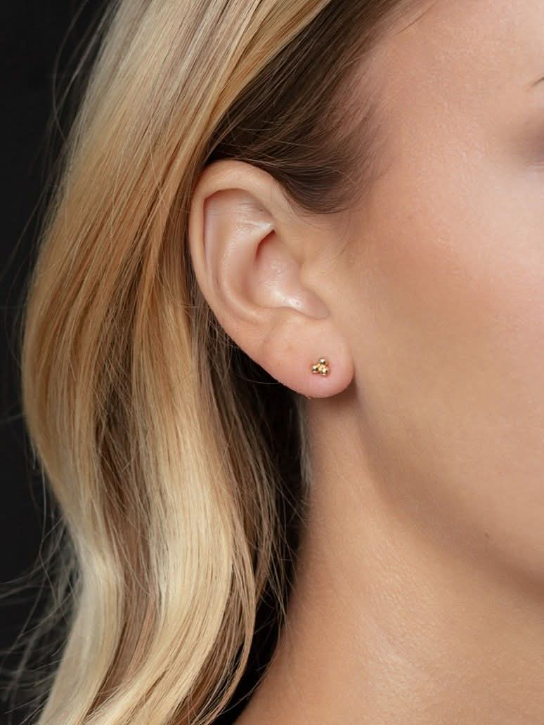 Close-up of an ear wearing a gold stud earring with blonde hair.