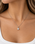 A close-up of a woman's neck and chest wearing a delicate silver chain necklace with a single round clear gemstone pendant.